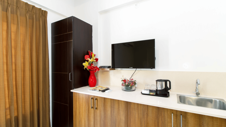 Hotel room dresser with a wall-mounted television, an electric kettle, and floral décor at Sanctum Suites Whitefield, Bangalore.