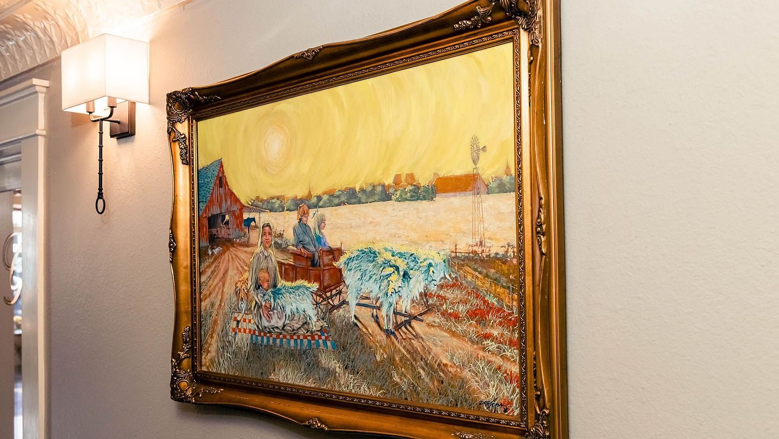 An  landscape painting with a  frame, mounted on a softly lit wall beside a vintage-style lamp.- The Grand Hotel & Ballroom, McKinney
