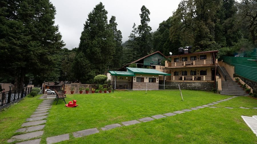 The Pavilion, Nainital's expansive green lawn area surrounded by dense forest, featuring stone pathways and traditional mountain architecture with red roofs.
