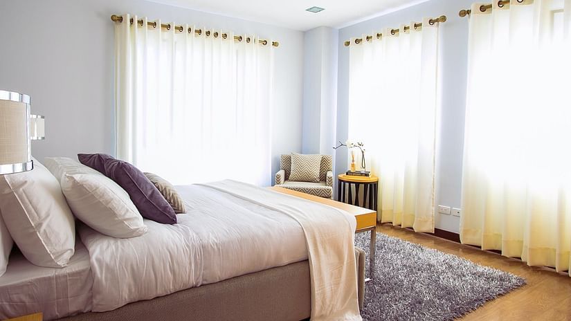 a well lit bedroom with multiple large windows and a bed with multiple pillows