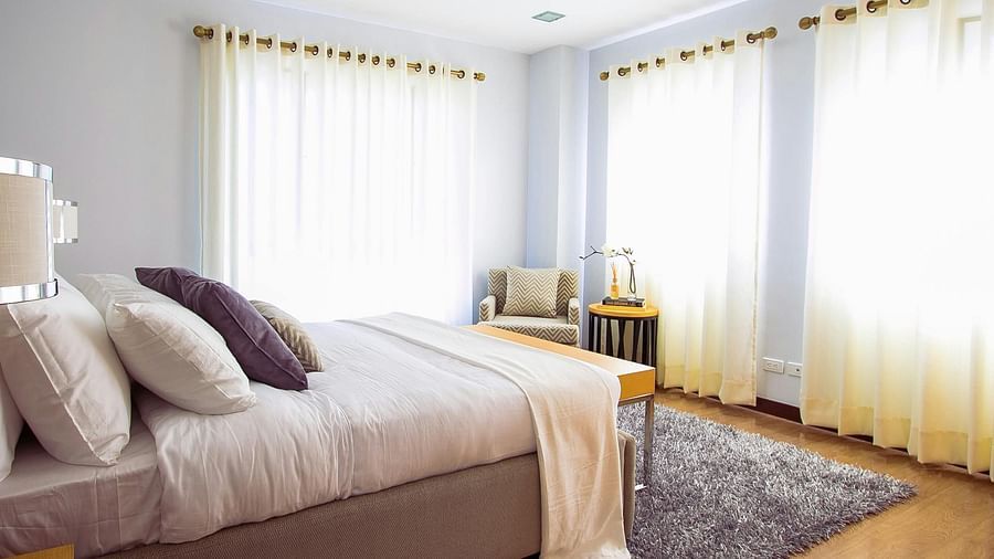 A bright and comfortable guest room featuring a large bed, natural light, and simple, clean decor.