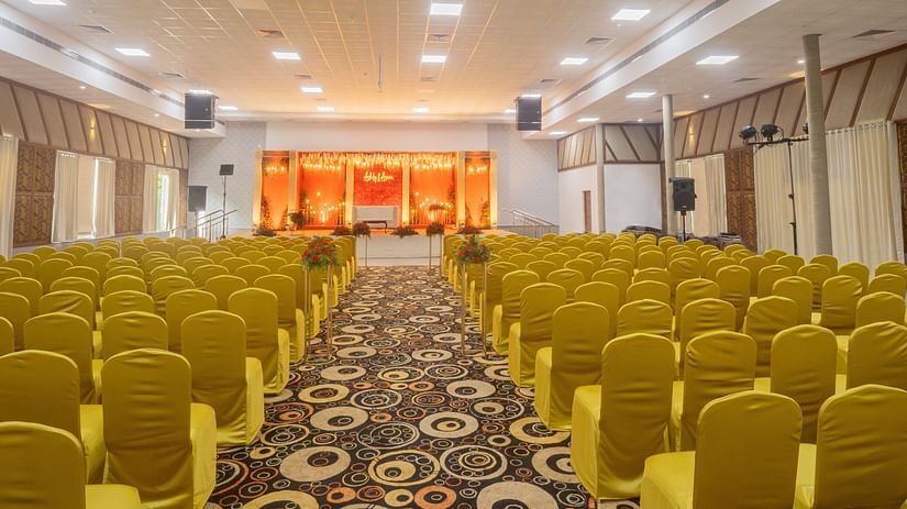 An image of a banquet hall with several chairs, speakers, cameras, and a stage set up on the front part of the hall- The Renai Cochin