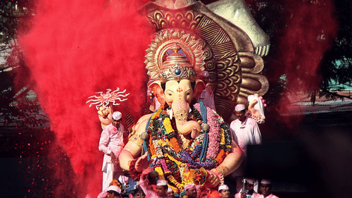 A statue of a deity covered in red powder during a celebration with people nearby.