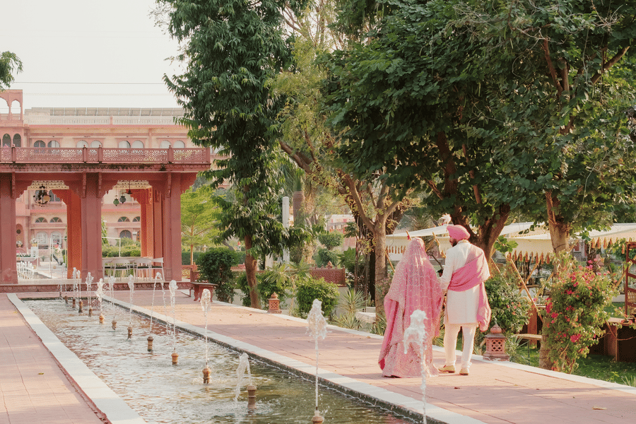 Bride Ritika and groom Jaswinder walking together beside long water garden at Umaid Palace wedding