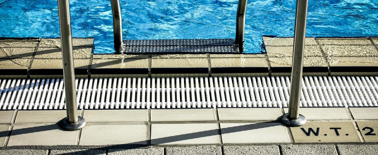 Two metal handrails lead into a swimming pool with blue water.