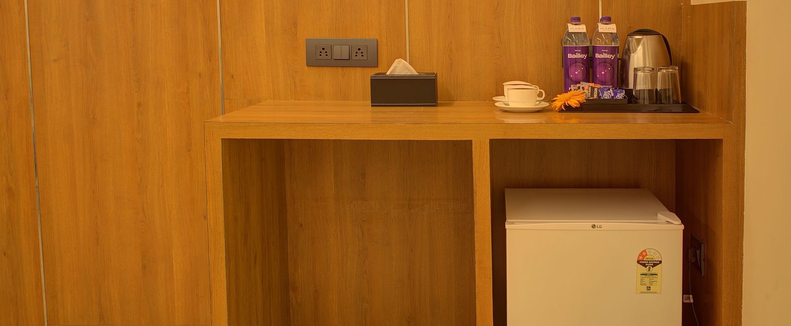 A wooden table in the corner of the Executive Suite with a mini fridge under it and a kettle with small refreshments on the table at Ilara Hotels & Spa, Tada.