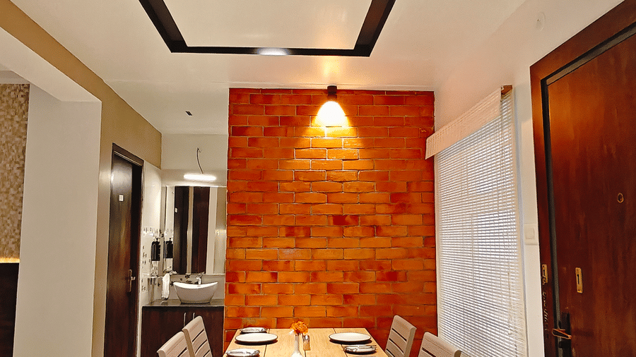 A wooden dining table with 6 chairs sits in a room with a bright orange feature wall at Bliss Casa Mila By Bergamont Hotels, Kodaikanal.
