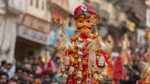 A colorful, traditional Gangaur idol being carried through the crowded historic streets of Udaipur during a festival.
