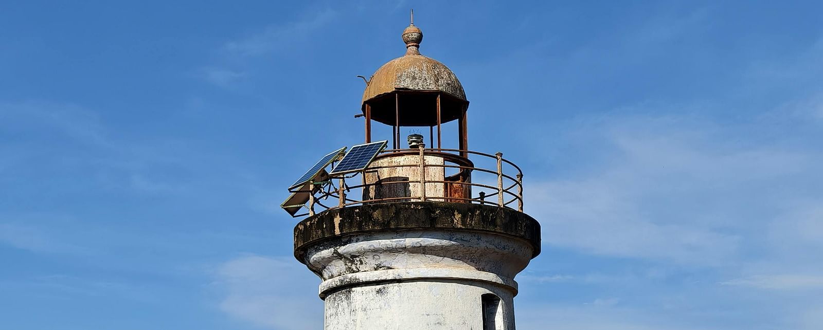 A tall, historic lighthouse with a white facade and black lantern room, standing against a clear blue sky.