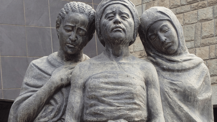 A stone memorial showing three figures standing close together.