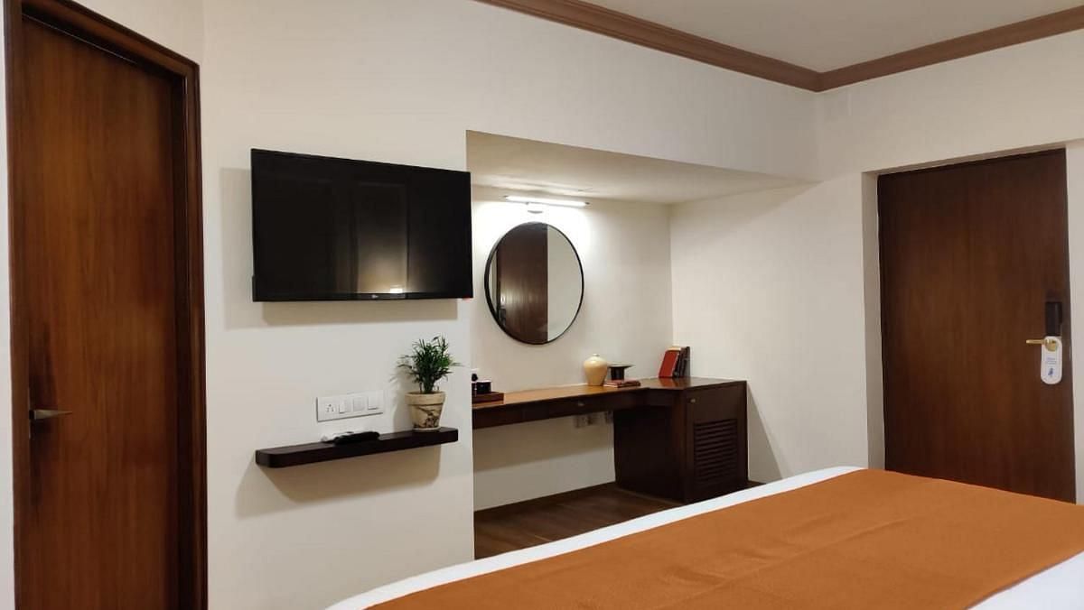 Luxury King Room featuring a bed with a brown runner, a side table, and a mirror at Nalapad Hotel Bangalore International.