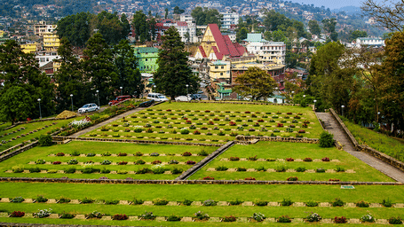 Terraced green lawn cemetery with graves overlooking a hillside town in the background.