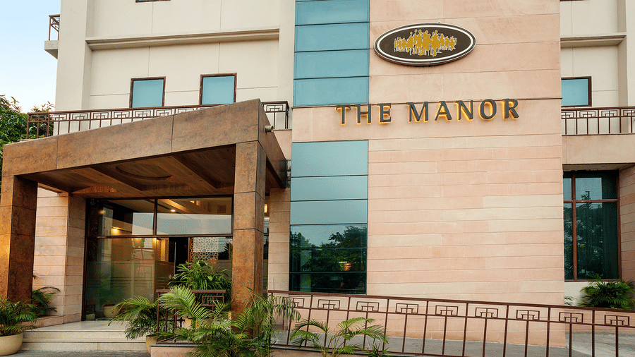 The facade of The Manor hotel, showcasing a modern entrance with potted plants and a clear blue sky above - The Manor, Bareilly