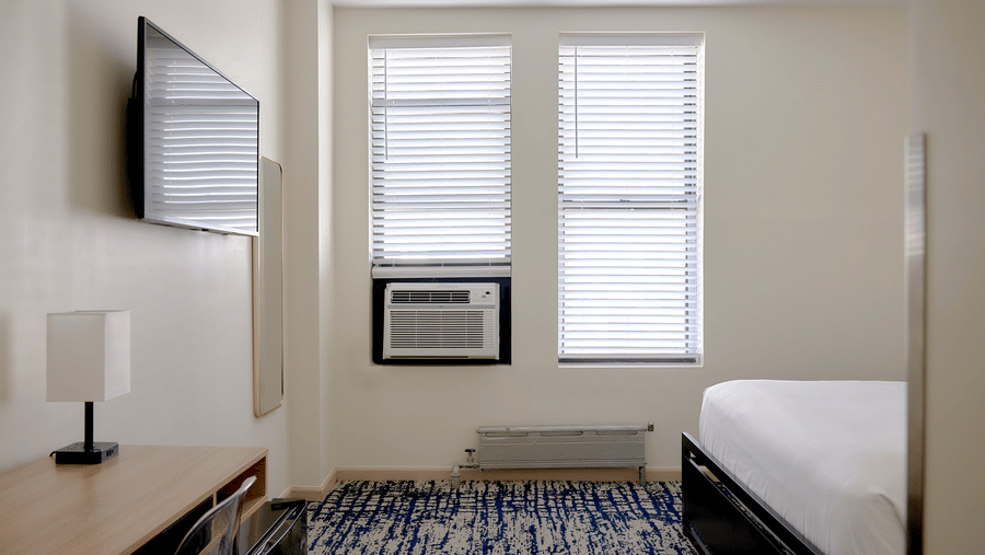 Bright room at Night Hotel Broadway with single bed, TV, air conditioner, and window.