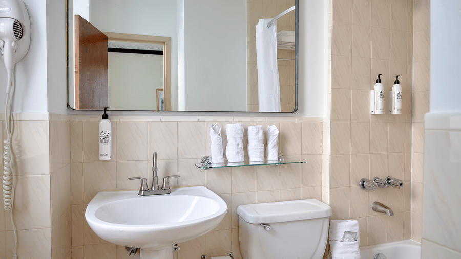 Bathroom at Night Hotel Broadway with sink, toilet, shower, and mirror over the counter.