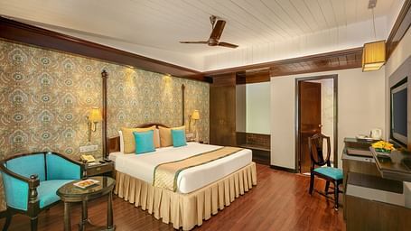 A cozy bedroom with a comfortable bed, warm lighting, and a view of the forest through a large window at Shervani Hilltop Nainital 