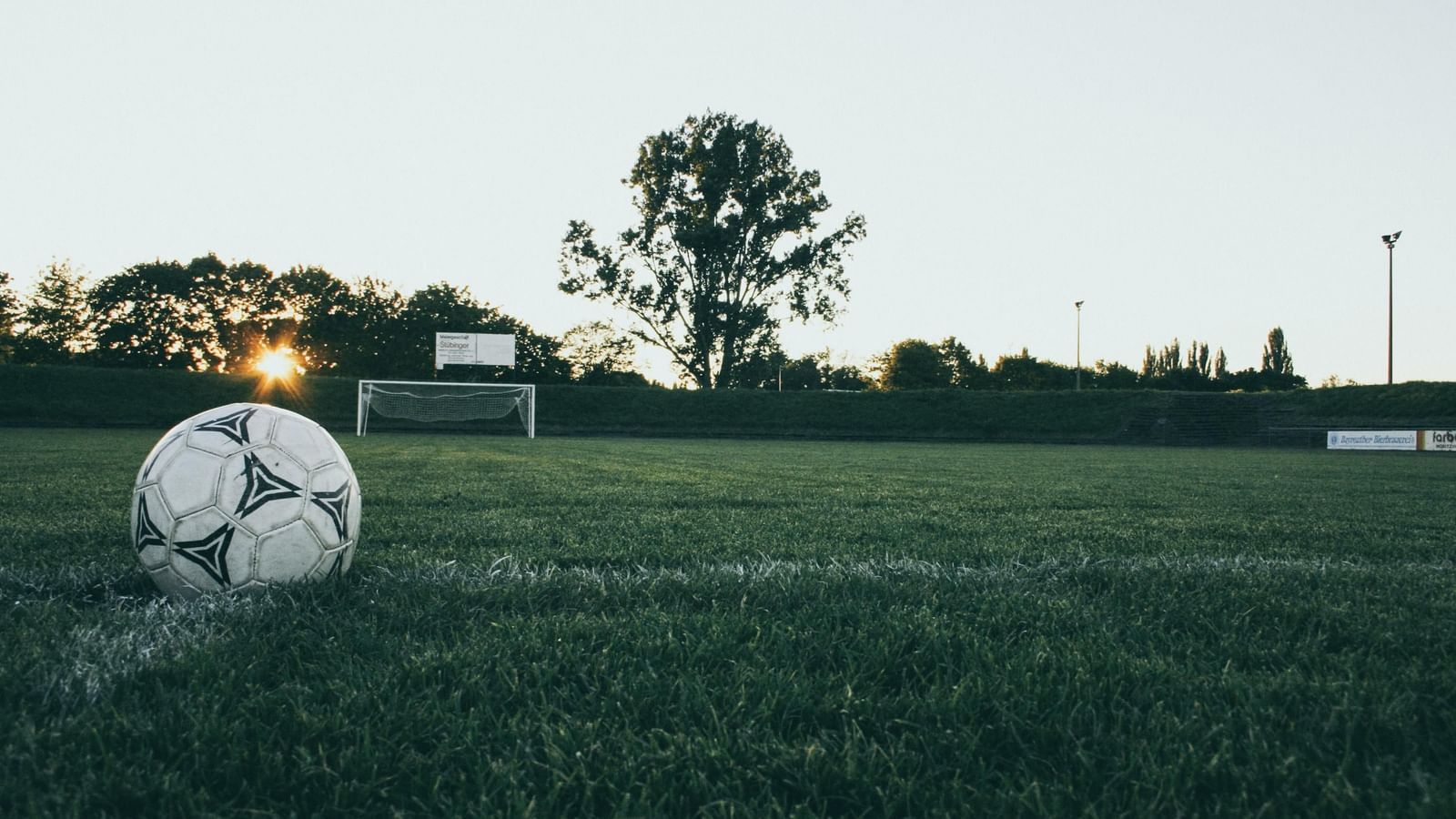 A white football lying on a grassy field with goalposts in the background.