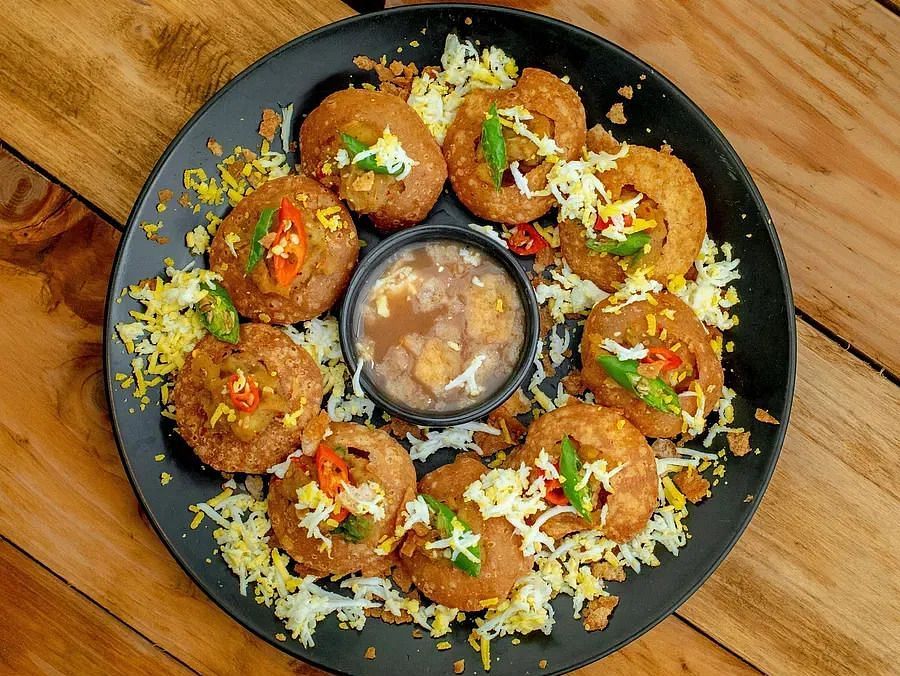 A plate of small, round snacks topped with various ingredients and sauces, arranged around a central bowl of dip, on a wooden surface.