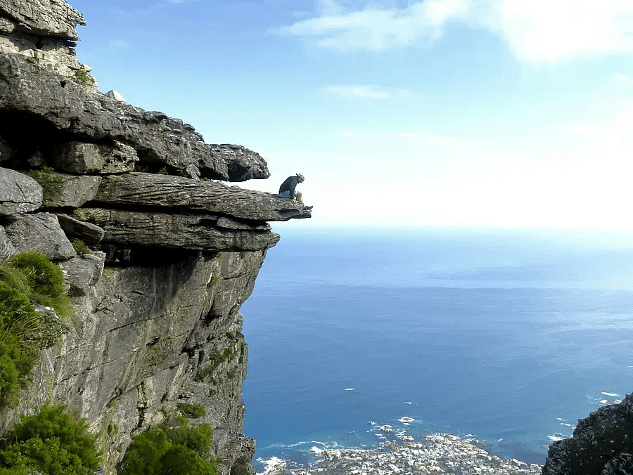 A person sitting on the edge of a cliff overlooking a coastal city and the ocean.