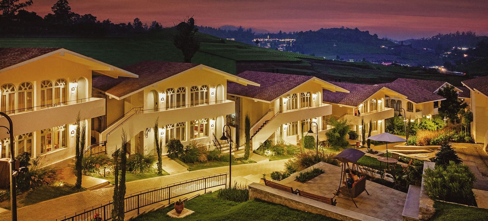 Aerial view of Mango Hill Shola, Ooty, with tiled-roof buildings arranged around a paved pathway and bordered by trees.