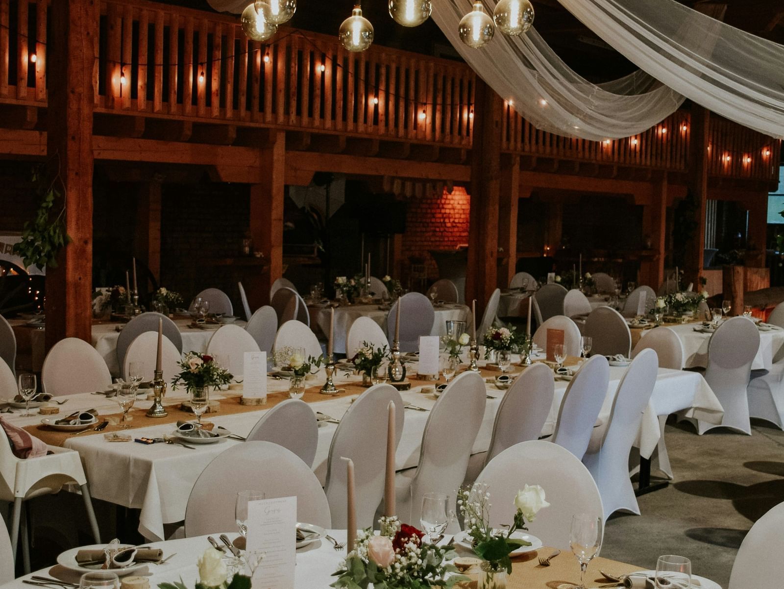 A banquet or event hall decorated for a formal occasion, with round dining tables and white drapes.