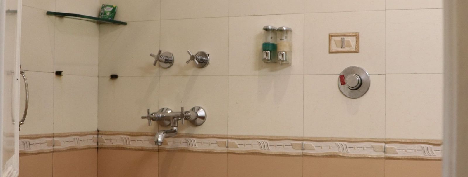 A bathroom with a white toilet, a shower area with a glass panel, and a tiled wall. - Hotel Diamond Plaza, Chandigarh.