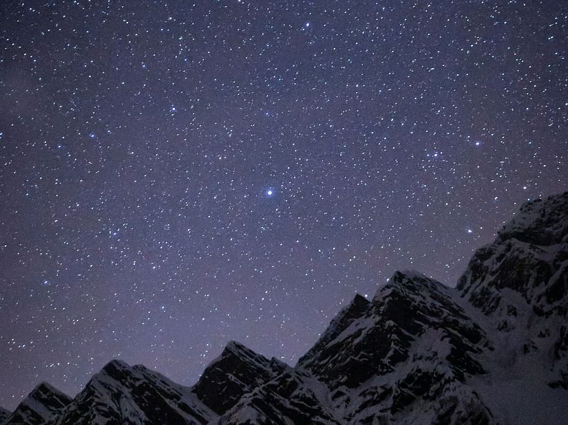 A view of the snow-capped himalayan mountains in the night with many stars in view.