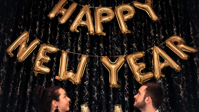 A couple holding drinks with happy new year made out of ballons on the wall