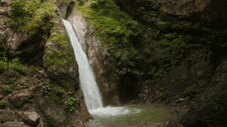 A person sitting on a rocky surface facing the cascading waterfall
