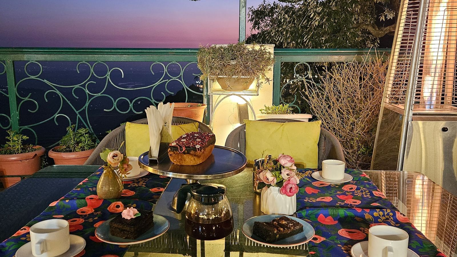 A terrace with tables set for dining under ambient lighting, offering sunset views at Mongas Hotel & Resort, Dalhousie 