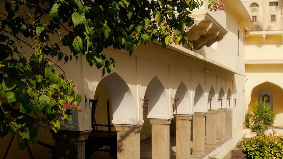 A sunlit section of Fort Barli with arched openings is partially obscured by vibrant foliage, blending architecture with nature.