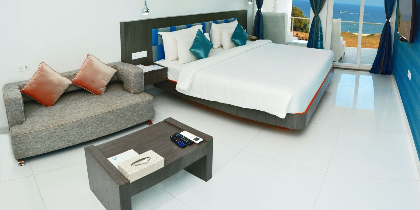 A clean, modern hotel bedroom with a large white bed, dark accent wall, and a small sitting area | Grande Chalet Sea View | Grande Bay Resort & Spa, Mamallapuram