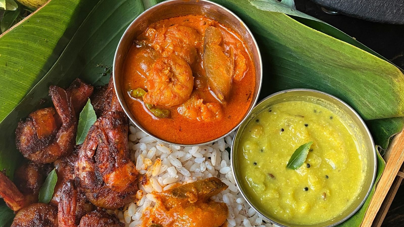 Top view shot of a plate featuring various sea food preparations served with steamed rice on a plate lined with banana leaf.
