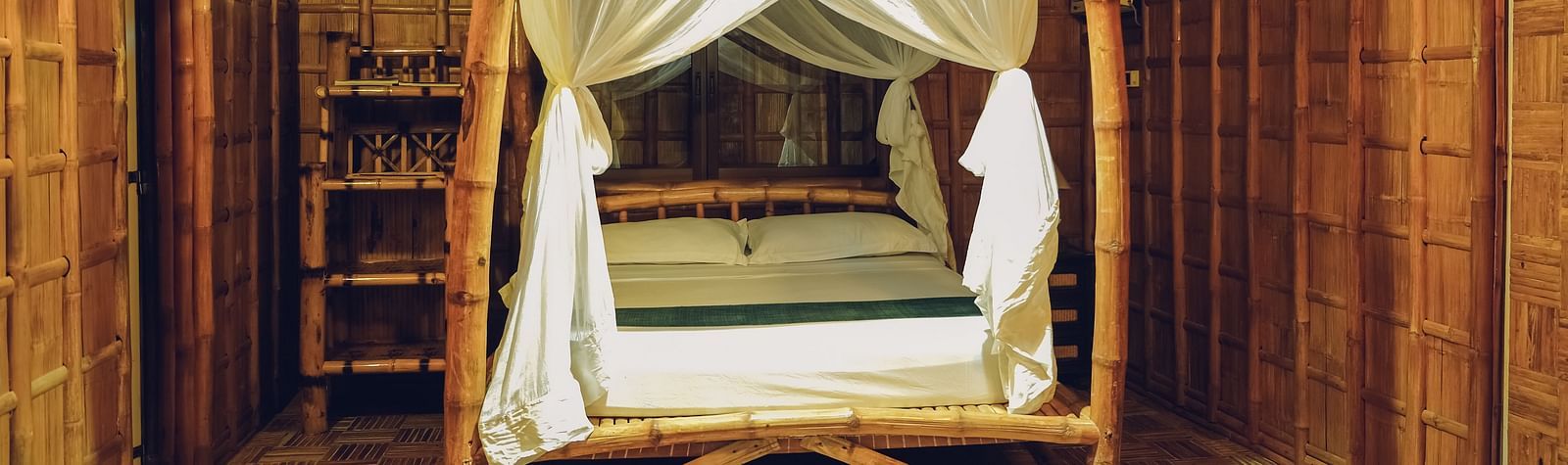 Standard Bamboo Suite at Flower Island Resort featuring a wooden canopy double bed,  bright lighting, and bamboo flooring.