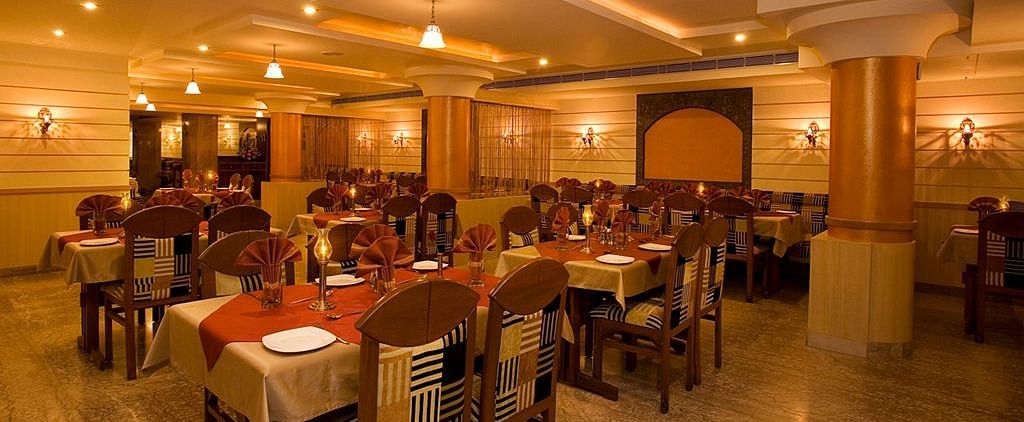 An image of a restaurant with several sets of chairs and table, and at one corner there is a reception desk - Hotel Pai Comforts JP Nagar Bangalore