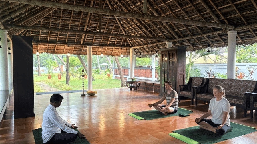 People practicing yoga postures on mats in a tranquil, open-air setting with a thatched roof  at Ayur On The Beach Nattika.