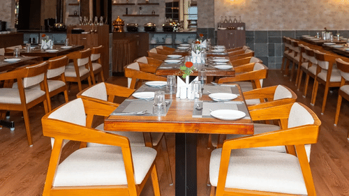 Well-arranged dining tables in Aromas restaurant at VITS Select, Bengaluru, with neat place settings and warm wooden interiors in full view.