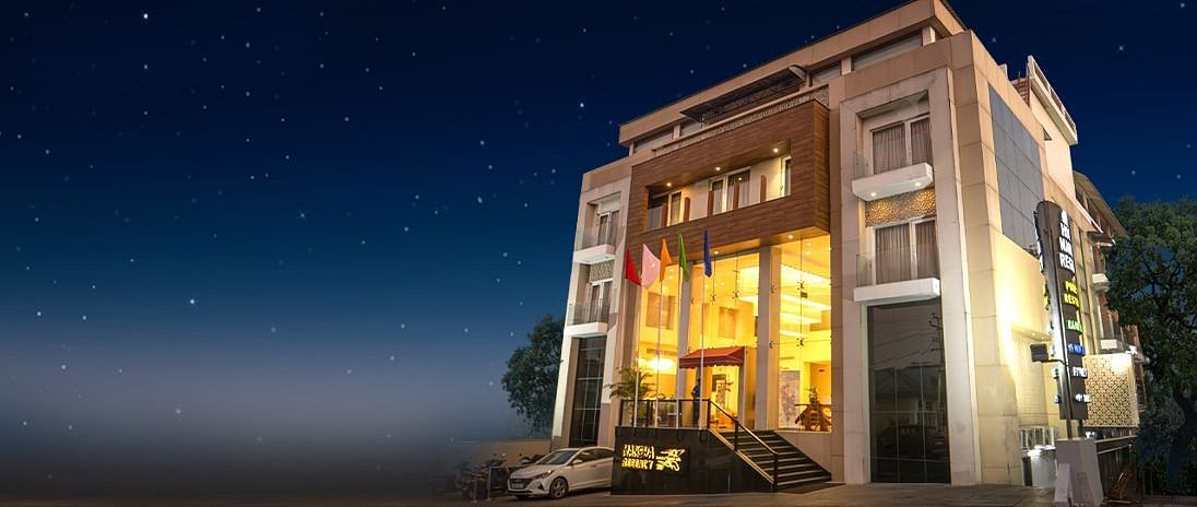 A multi-storey building with illuminated windows and a prominent entrance stands under a dark, star-filled night sky - Mansha Regency, Port Blair