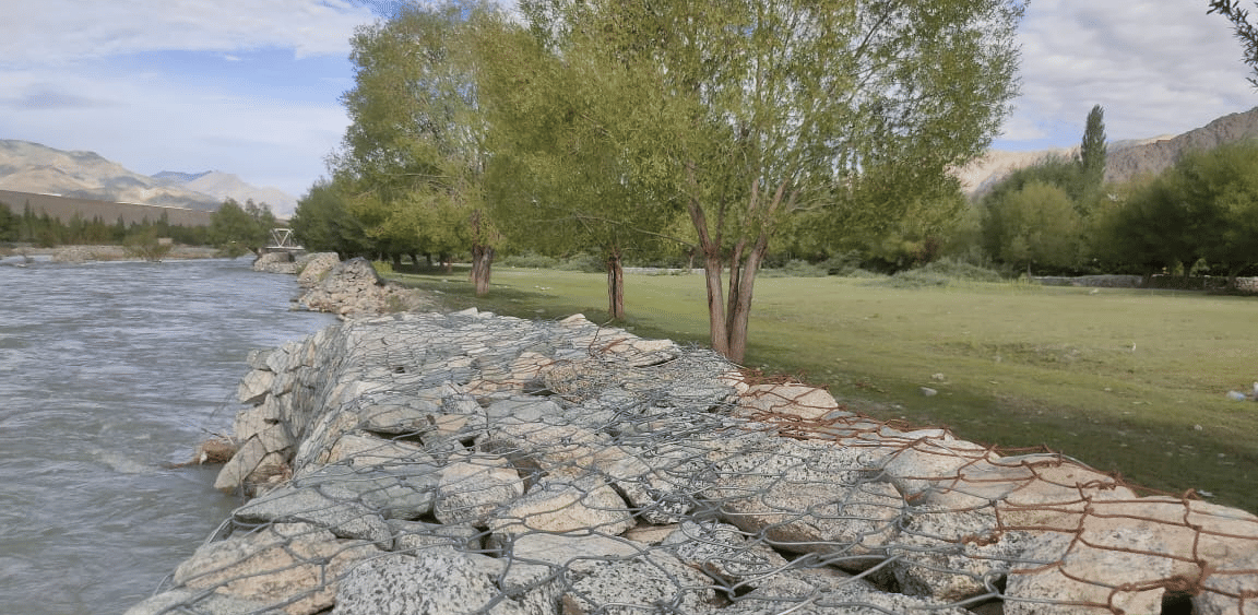 A sturdy stone-paved embankment running alongside a wide, fast-flowing river at Indus Serenity Retreat.