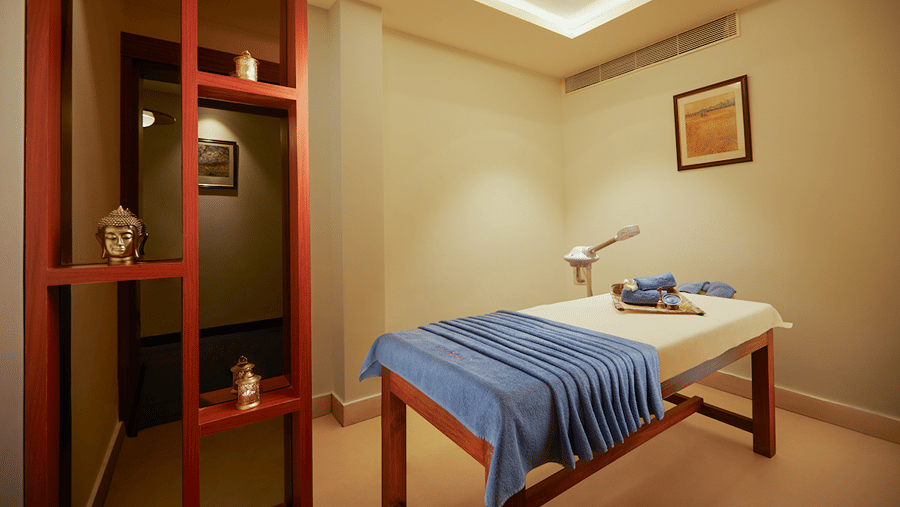 A massage table with a folded cloth in a room with a red-framed partition and a small picture on the wall.