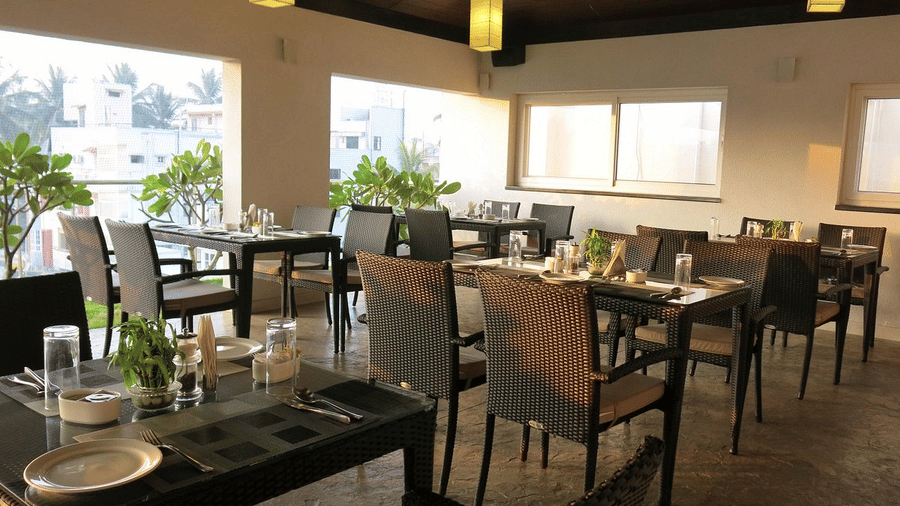 The seating area in Tree Top Restaurant with dark wicker tables and chairs under hanging warm lantern lights at Temple Tree Hotel, Bangalore.