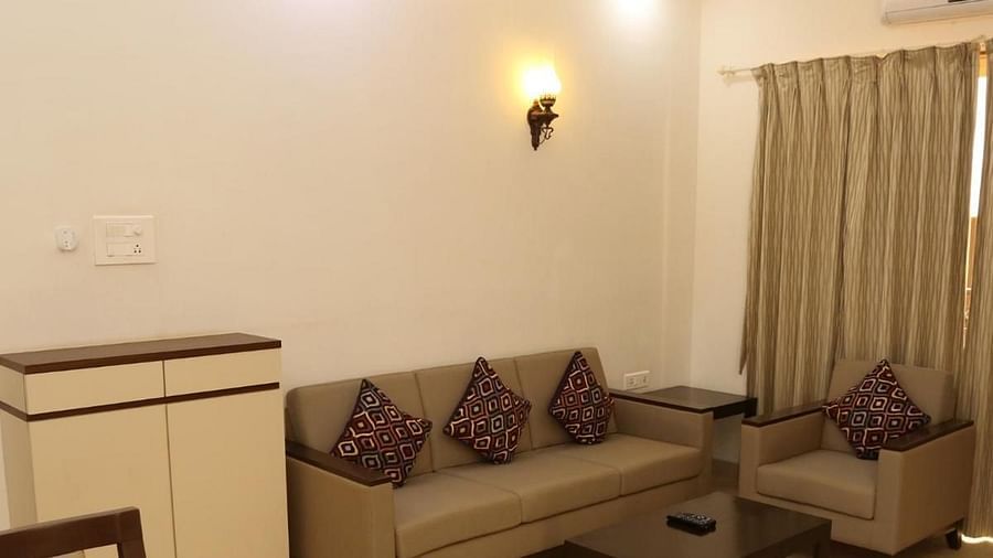 Cushioned sofa against the wall with a short sideboard on one side and windows with curtains on the other, along with a small table in front at La Vida Studio Inn
