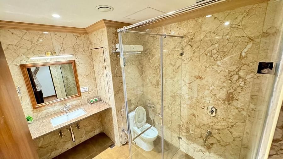 The bathroom of a Classic Twin Room featuring a glass-enclosed shower area with a toilet inside, and a vanity with a sink and mirror. - Nalapad Hotel Bangalore International