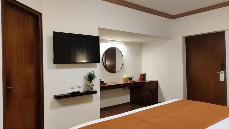 Luxury King Room featuring a bed with a brown runner, a side table, and a mirror at Nalapad Hotel Bangalore International.