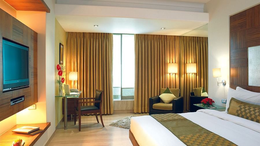 Image of a the executive room featuring a king size bed, a study table and chair, flat screen television, and an expansive window with golden curtains. | Mirage Hotel