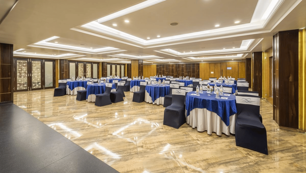 A conference room arranged with round tables draped in blue and white tablecloths, and warm lighting - The Citrine, Bangalore