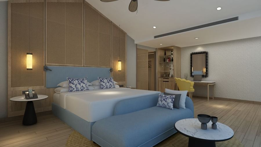 Interiors of Havelock Water Villa featuring a double size bed, a couch attached to the bed, centre table, bedside table and hanging lamps on either side of the bed. The villa also has a wardrobe, workdesk and chair, and a mirror on the wall.