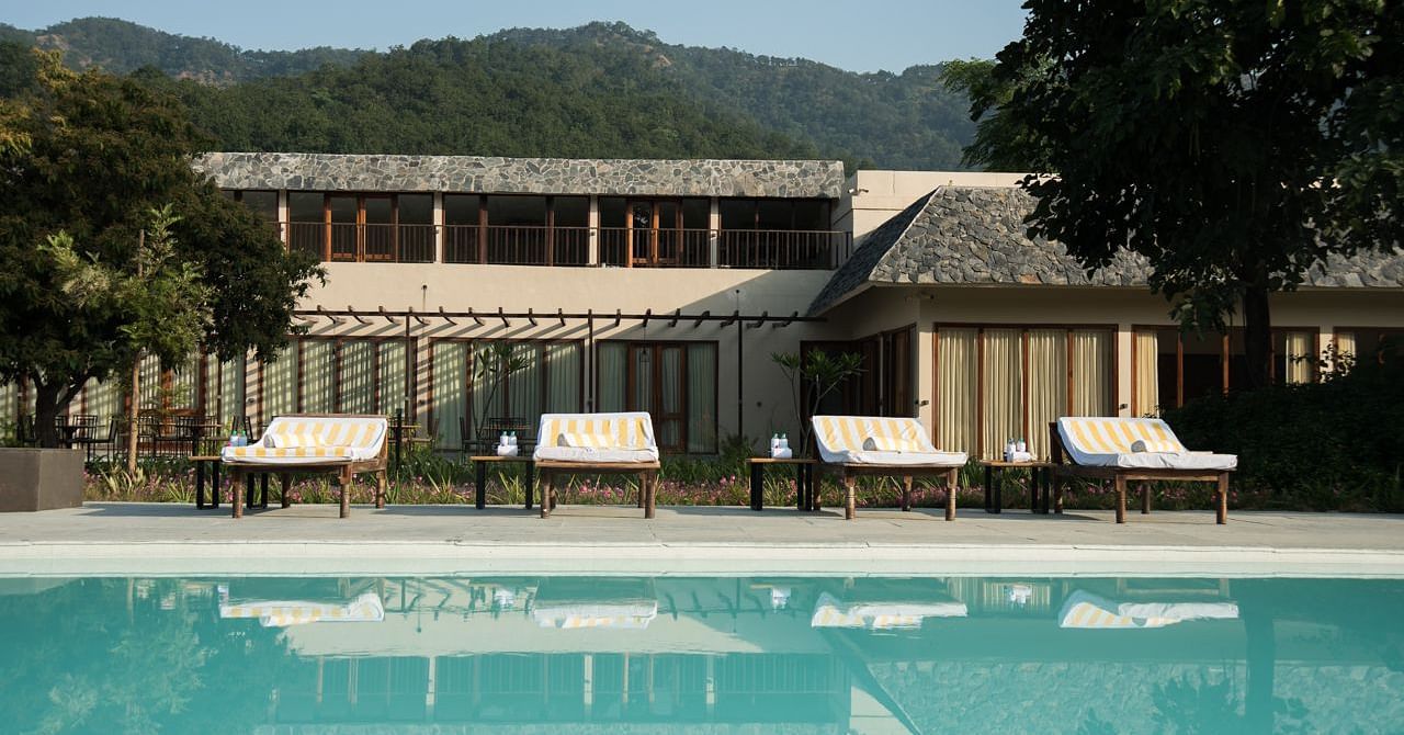 The outdoor swimming pool at Saraca Resort & Spa Corbett with lounging chairs placed in the backdrop