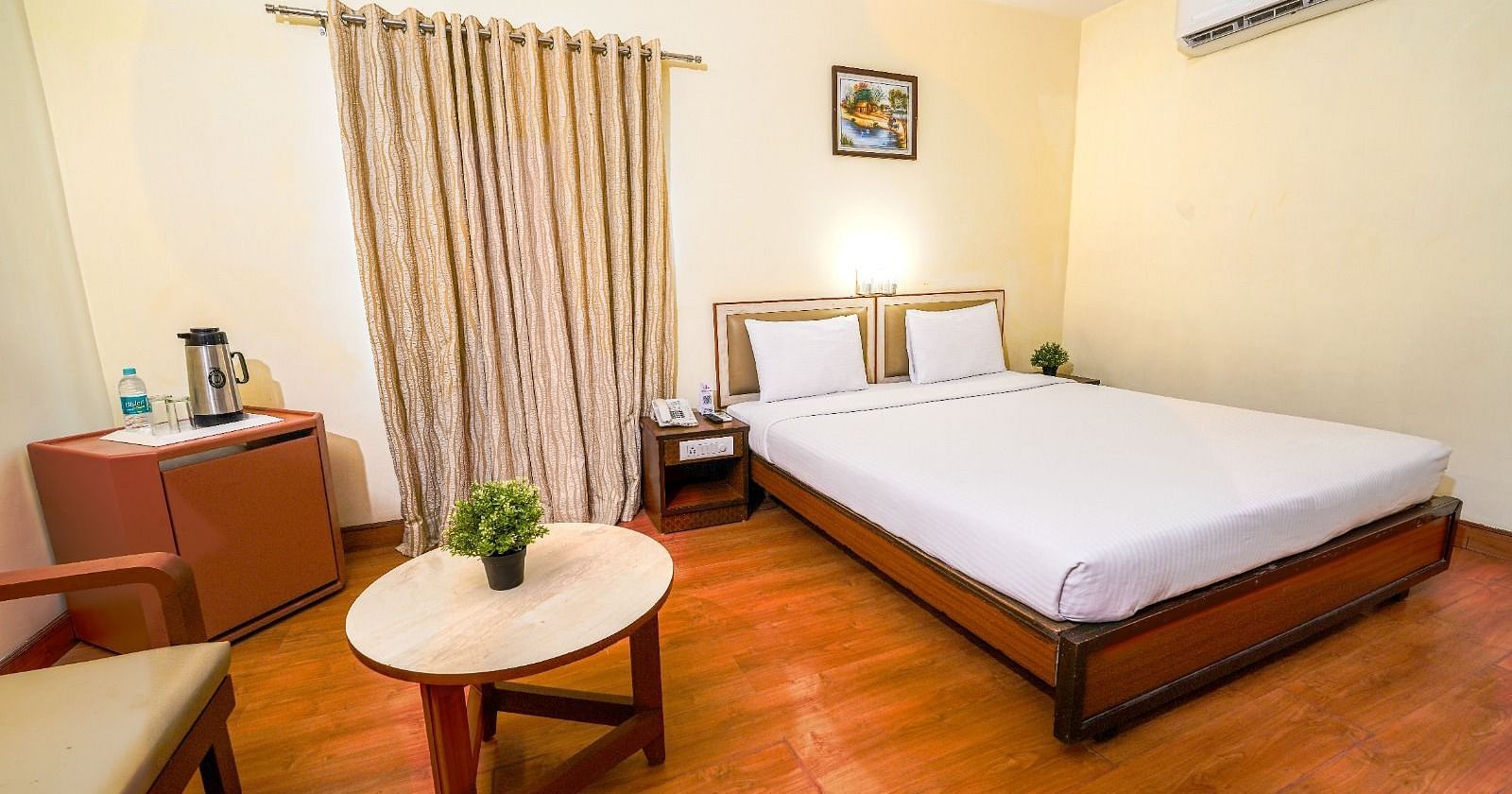 Bright hotel room with a double bed, wooden flooring, and a seating area by the window in Hyderabad near Ramoji Film City.
