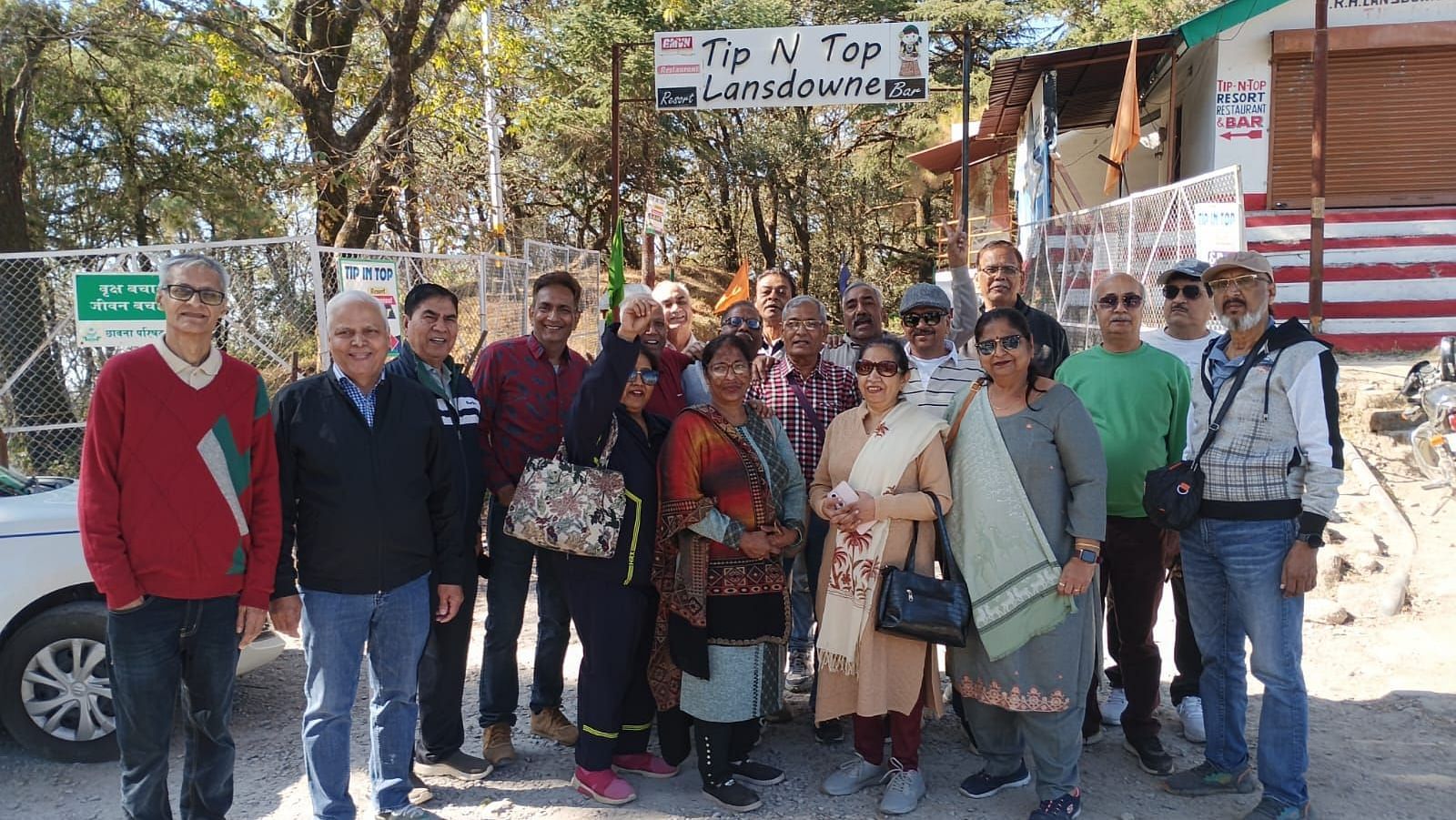 A group of people standing together in front of the 'Tip N Top Lansdowne' sign, smiling and posing for the photo. The background features trees and a building.